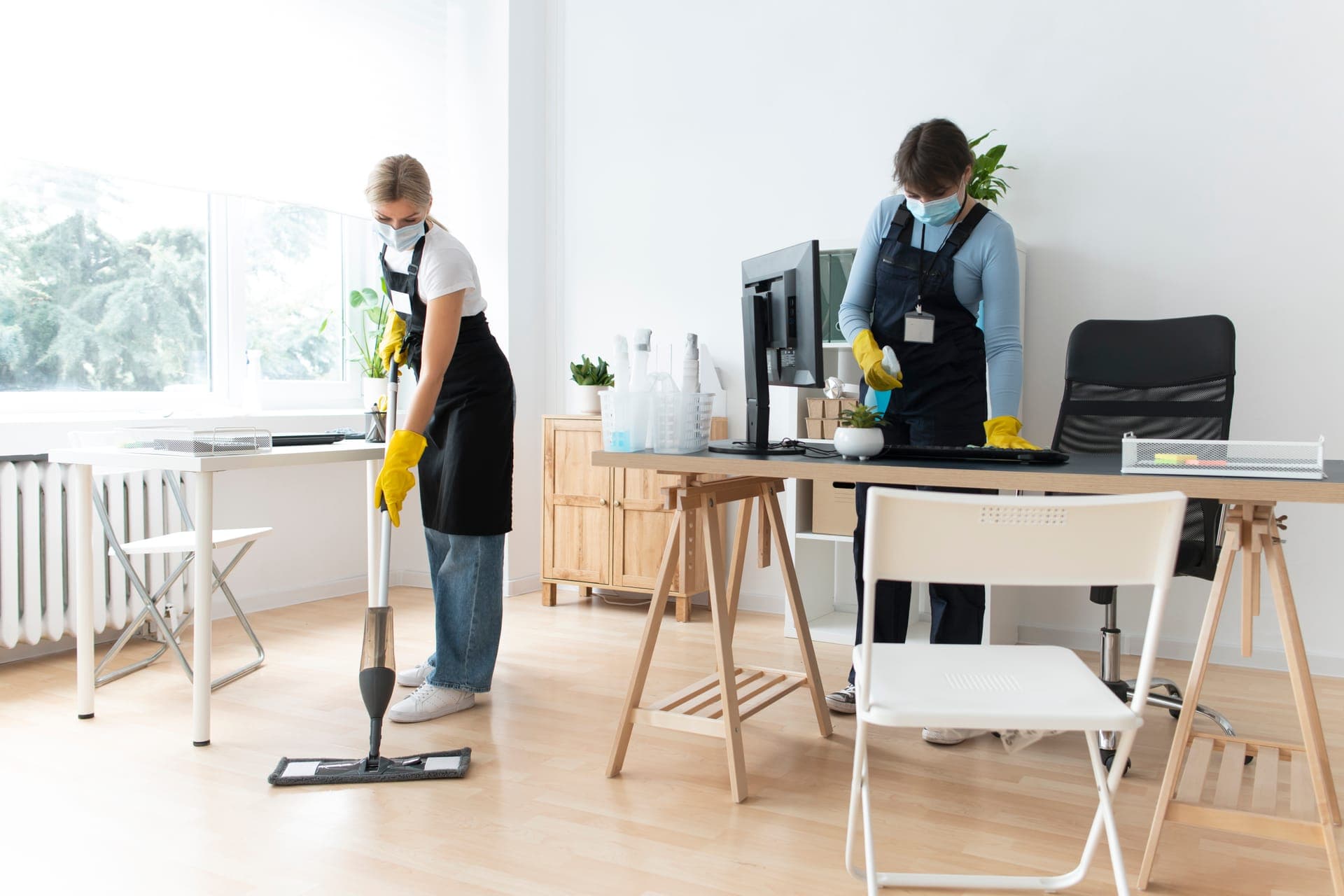 Two uniformed OLAH Services cleaners mopping the floor and disinfecting desks in a bright commercial office